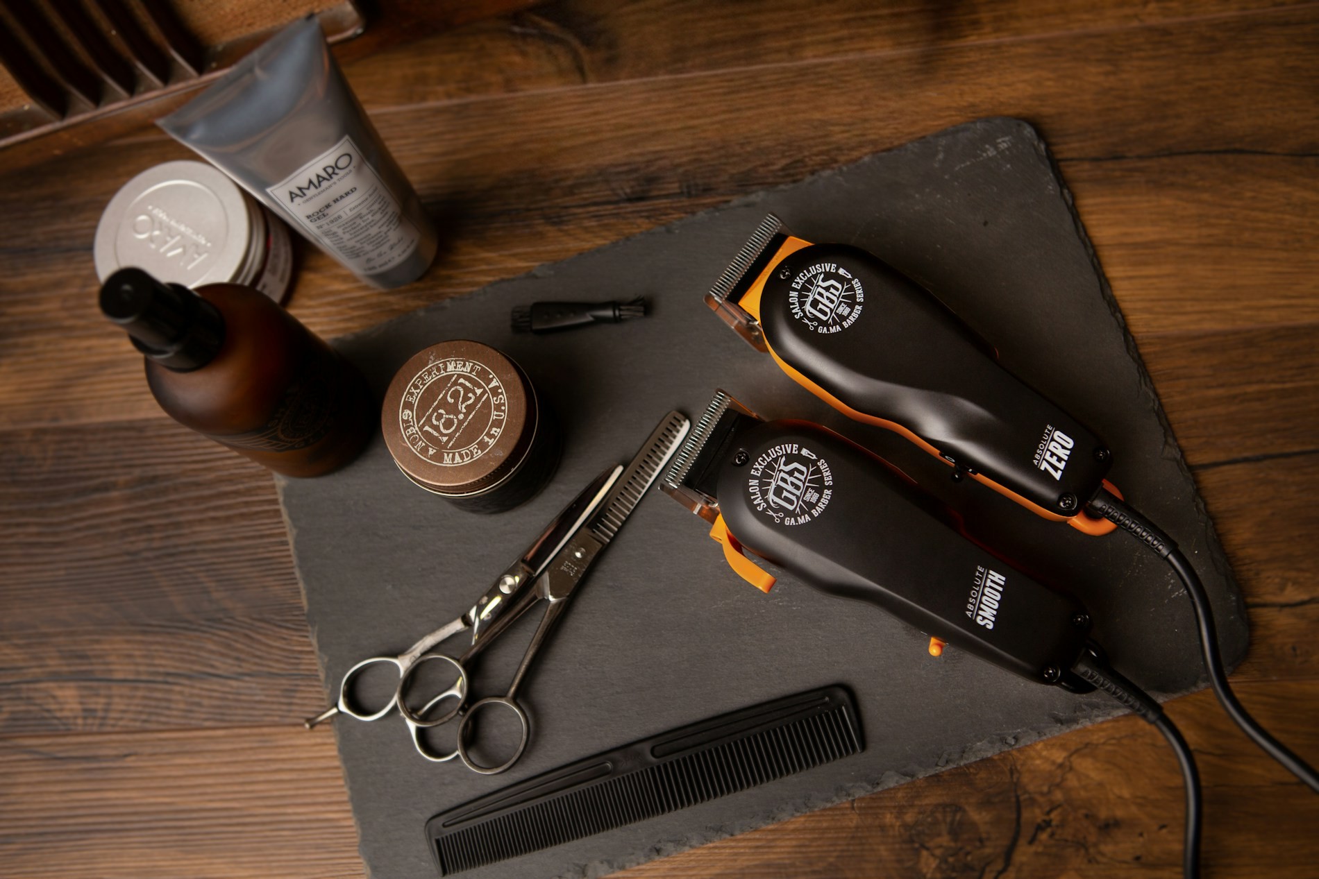 Premium grooming tools — clippers, scissors, comb and beard products laid out on dark slate